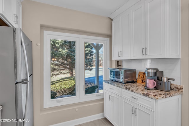 kitchen with backsplash, white cabinets, light stone counters, and stainless steel refrigerator