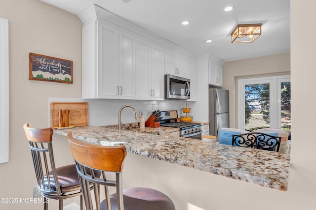 kitchen with a kitchen bar, sink, white cabinetry, stainless steel appliances, and light stone counters