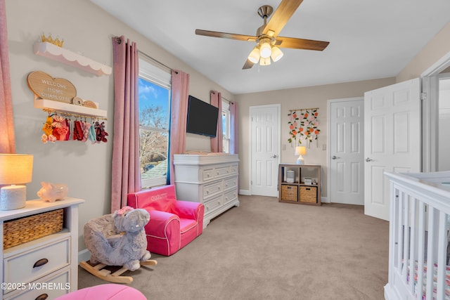 bedroom featuring light carpet, ceiling fan, and a crib