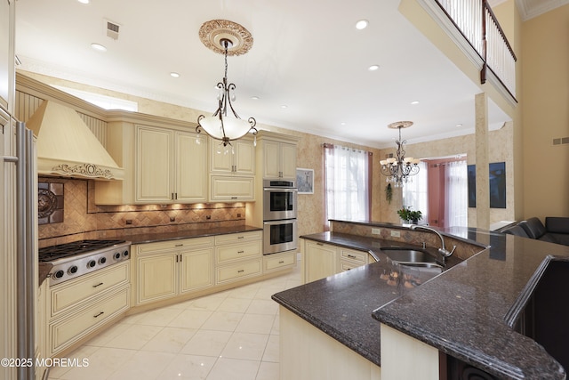 kitchen with cream cabinetry, appliances with stainless steel finishes, hanging light fixtures, custom range hood, and sink