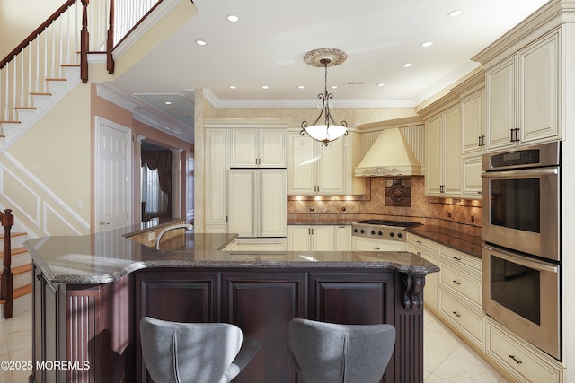 kitchen featuring premium range hood, stainless steel appliances, cream cabinets, and decorative light fixtures