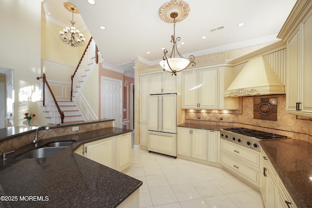 kitchen featuring cream cabinets, stainless steel gas stovetop, dark stone countertops, and pendant lighting