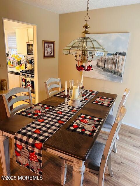 dining room with an inviting chandelier, a textured ceiling, and light wood-type flooring