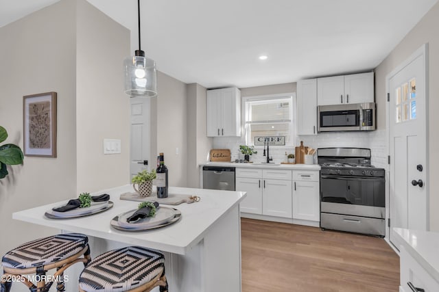 kitchen with tasteful backsplash, white cabinetry, stainless steel appliances, and hanging light fixtures