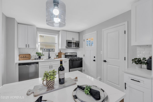 kitchen with hanging light fixtures, white cabinets, appliances with stainless steel finishes, and tasteful backsplash