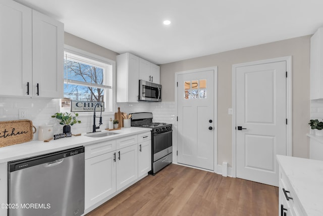 kitchen featuring appliances with stainless steel finishes, backsplash, white cabinets, light hardwood / wood-style flooring, and sink