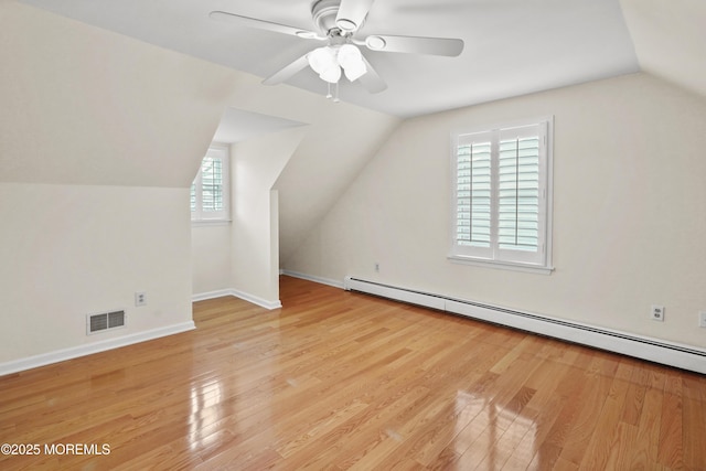 additional living space with ceiling fan, a baseboard heating unit, vaulted ceiling, and light wood-type flooring