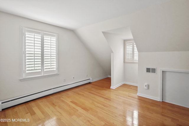 additional living space with a baseboard heating unit, vaulted ceiling, and light hardwood / wood-style flooring