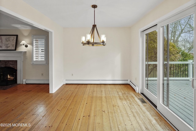 unfurnished dining area featuring a brick fireplace, baseboard heating, light hardwood / wood-style floors, and a notable chandelier