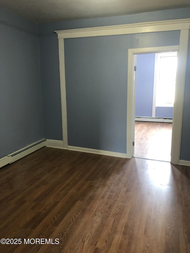 empty room featuring baseboard heating and dark wood-type flooring