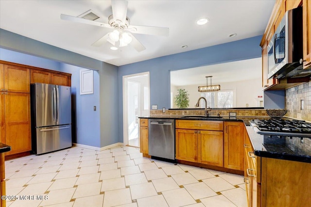 kitchen with pendant lighting, brown cabinets, appliances with stainless steel finishes, a sink, and a peninsula