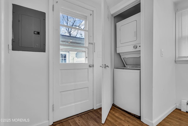 washroom featuring stacked washer and dryer, electric panel, a baseboard heating unit, and wood-type flooring