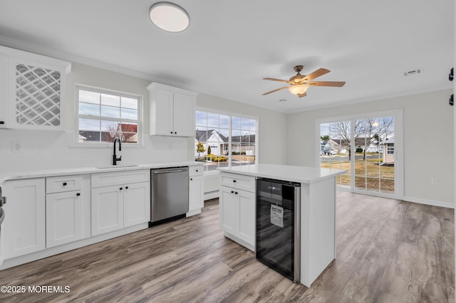 kitchen featuring beverage cooler, white cabinets, sink, stainless steel dishwasher, and light hardwood / wood-style flooring