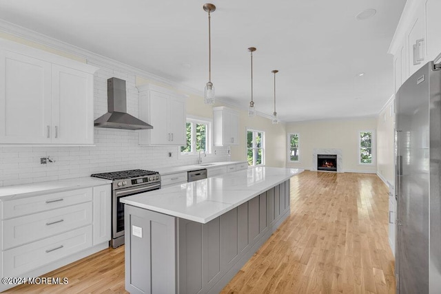 kitchen with wall chimney range hood, a kitchen island, pendant lighting, sink, and appliances with stainless steel finishes