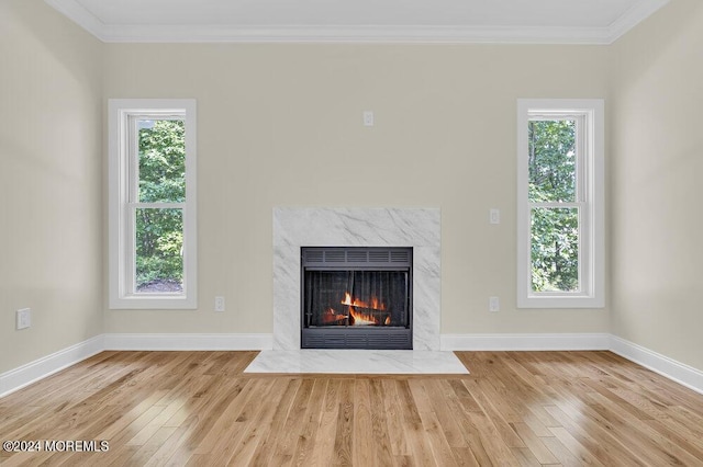 unfurnished living room with light hardwood / wood-style flooring, a high end fireplace, ornamental molding, and a healthy amount of sunlight