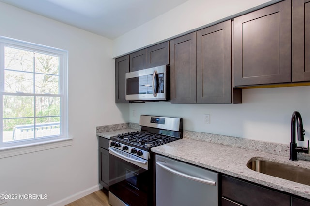 kitchen featuring appliances with stainless steel finishes, sink, light stone counters, and dark brown cabinetry