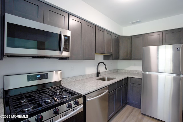 kitchen with light stone countertops, sink, dark brown cabinetry, and appliances with stainless steel finishes