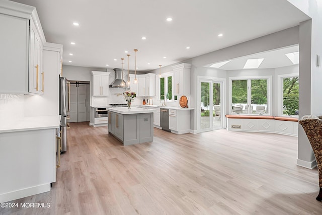 kitchen with white cabinets, a center island, wall chimney exhaust hood, a skylight, and hanging light fixtures