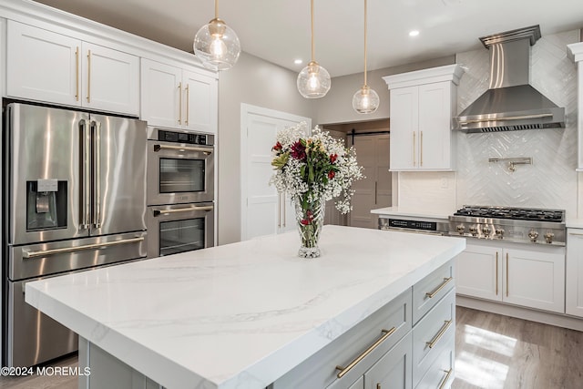 kitchen featuring white cabinets, wall chimney range hood, stainless steel appliances, tasteful backsplash, and a barn door