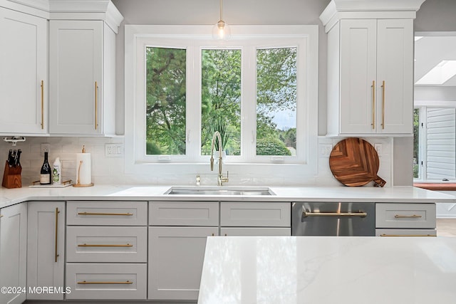 kitchen featuring light stone countertops, sink, backsplash, hanging light fixtures, and stainless steel dishwasher