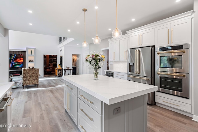 kitchen with light hardwood / wood-style floors, a kitchen island, pendant lighting, stainless steel appliances, and white cabinets