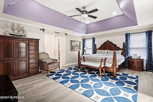 bedroom featuring light wood-type flooring, ceiling fan, ornamental molding, and a tray ceiling