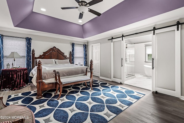 bedroom featuring ceiling fan, a barn door, ensuite bath, a tray ceiling, and hardwood / wood-style flooring