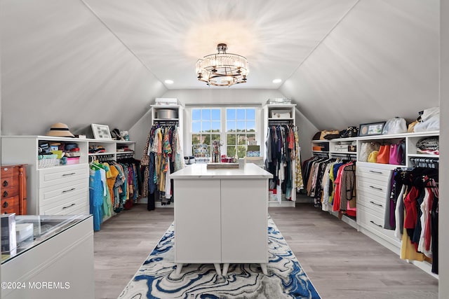 walk in closet with light hardwood / wood-style flooring, a chandelier, and vaulted ceiling