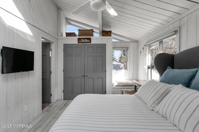 bedroom featuring lofted ceiling, ceiling fan, wood walls, light hardwood / wood-style floors, and a closet