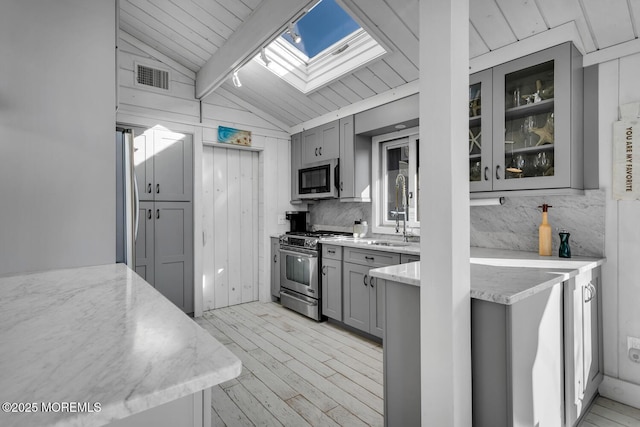 kitchen featuring appliances with stainless steel finishes, gray cabinetry, lofted ceiling with skylight, and sink