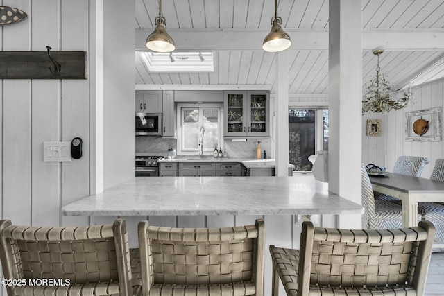 kitchen with hanging light fixtures, decorative backsplash, gray cabinets, and stainless steel appliances