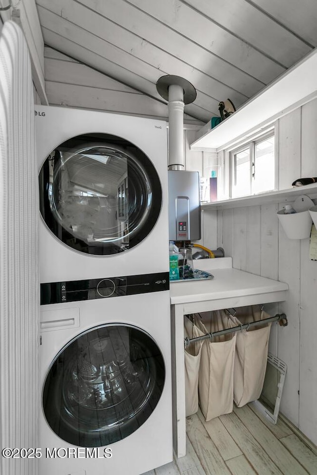 laundry area featuring light wood-type flooring, stacked washer and clothes dryer, wood walls, and water heater