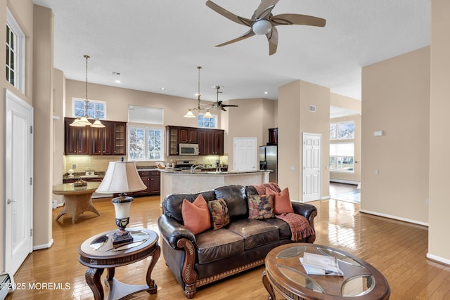 living room with a baseboard heating unit, ceiling fan, light hardwood / wood-style flooring, and a high ceiling