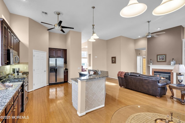 kitchen with stainless steel appliances, decorative light fixtures, dark stone countertops, dark brown cabinetry, and sink