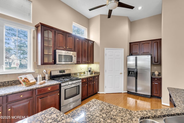 kitchen with a towering ceiling, stainless steel appliances, tasteful backsplash, light hardwood / wood-style floors, and ceiling fan