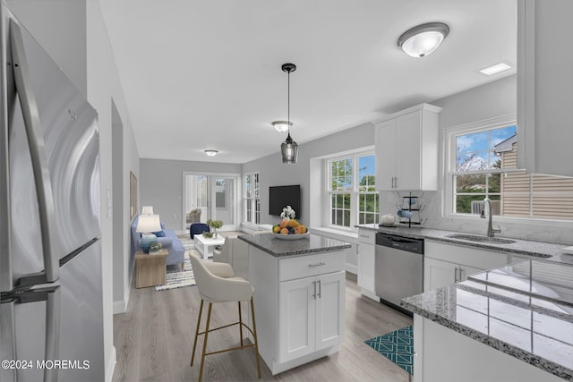 kitchen with white cabinets, appliances with stainless steel finishes, a kitchen island, light wood-type flooring, and light stone counters