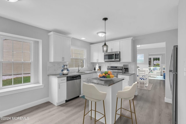 kitchen with hanging light fixtures, white cabinets, stainless steel appliances, and a kitchen island