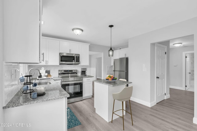 kitchen featuring appliances with stainless steel finishes, hanging light fixtures, a kitchen island, white cabinets, and sink