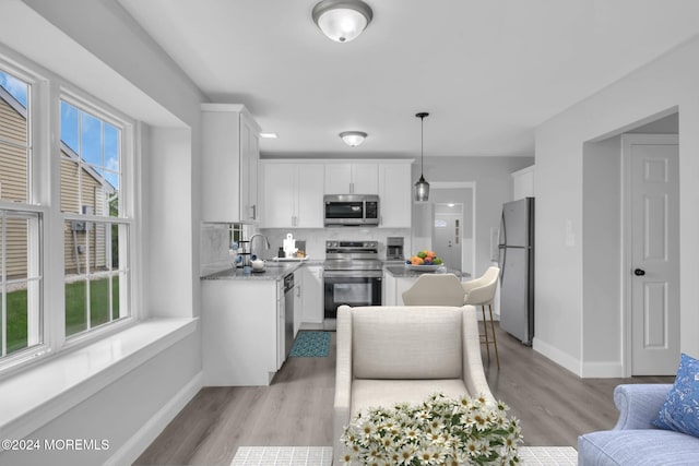 kitchen featuring white cabinetry, stainless steel appliances, a healthy amount of sunlight, and hanging light fixtures