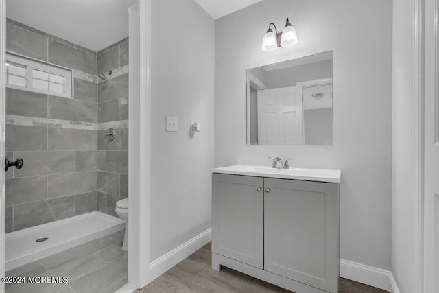 bathroom featuring vanity, toilet, hardwood / wood-style flooring, and tiled shower