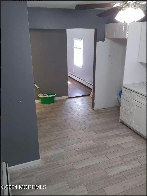 interior space with ceiling fan, white cabinets, baseboard heating, and light hardwood / wood-style floors