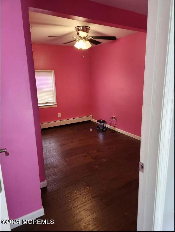 empty room with a baseboard heating unit, dark wood-type flooring, and ceiling fan