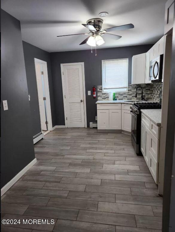 kitchen with a baseboard heating unit, gas range, white cabinets, and sink