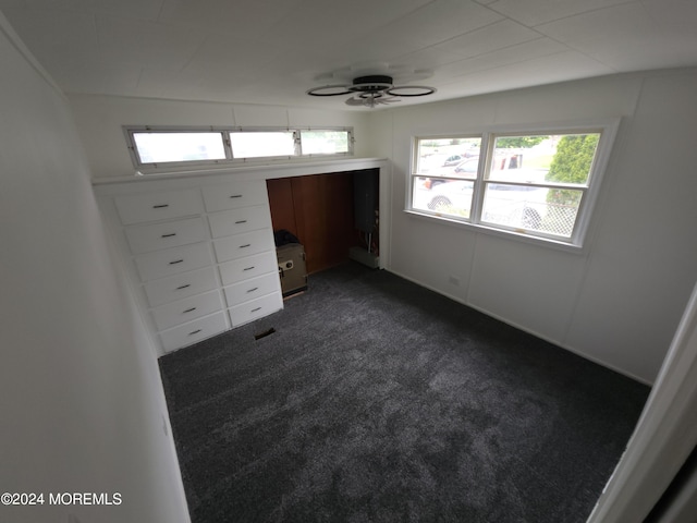 unfurnished bedroom featuring ceiling fan, dark carpet, and multiple windows