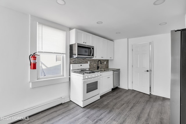 kitchen with white cabinetry, appliances with stainless steel finishes, backsplash, a baseboard radiator, and light wood-type flooring