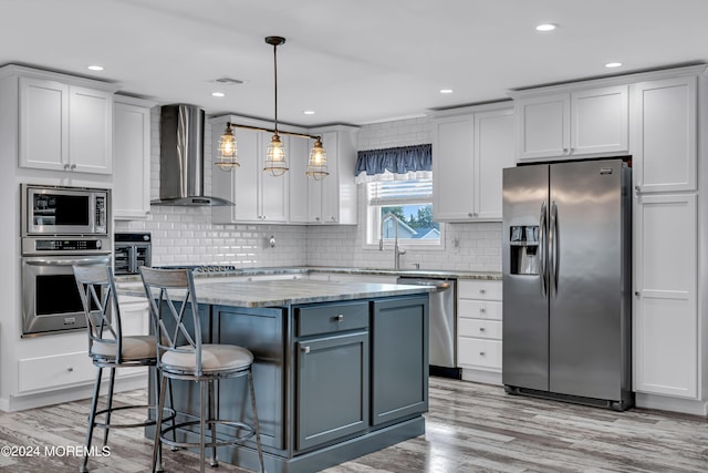 kitchen with decorative light fixtures, wall chimney range hood, a center island, stainless steel appliances, and light stone counters