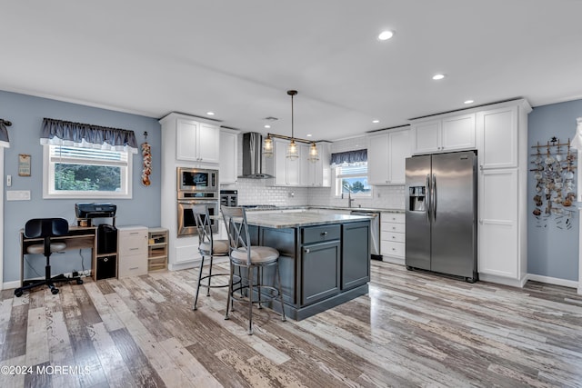 kitchen featuring hanging light fixtures, appliances with stainless steel finishes, a kitchen breakfast bar, white cabinets, and wall chimney exhaust hood