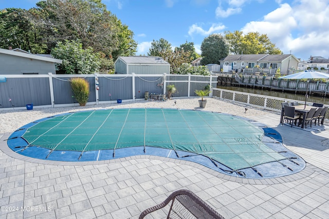 view of pool with a water view, a storage unit, and a patio area