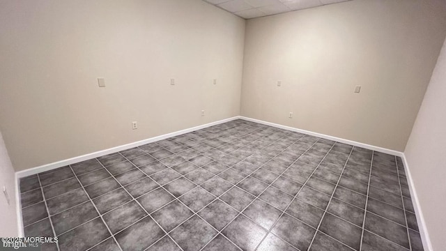 empty room with dark tile patterned flooring and a drop ceiling