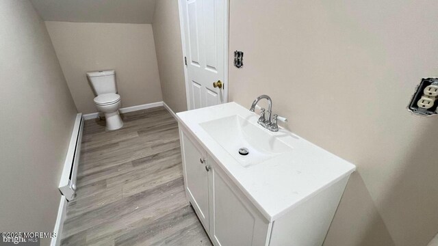 bathroom featuring hardwood / wood-style floors, a baseboard heating unit, vanity, and toilet